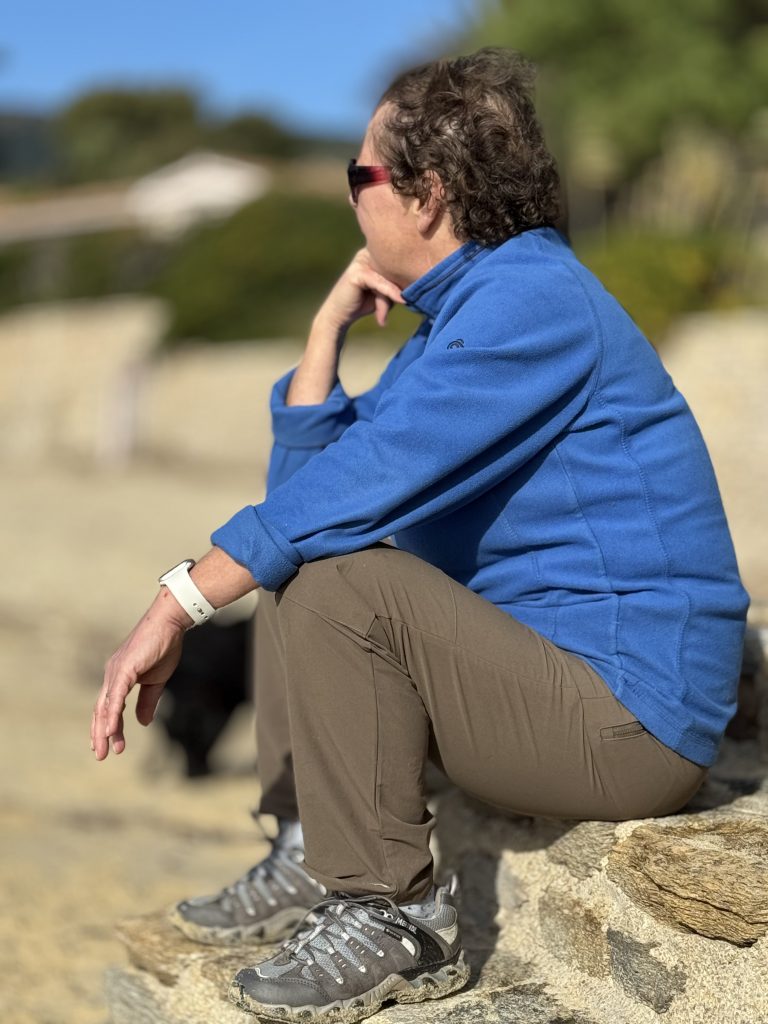 Pip sitting on a step on a beach in the sun looking chilled