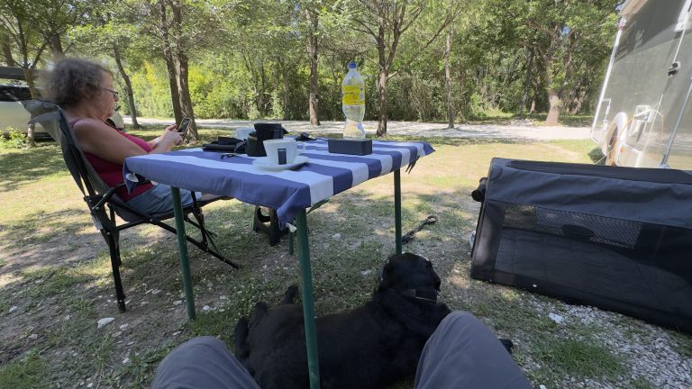 Couple with a black Labrador sat under a campervan awining